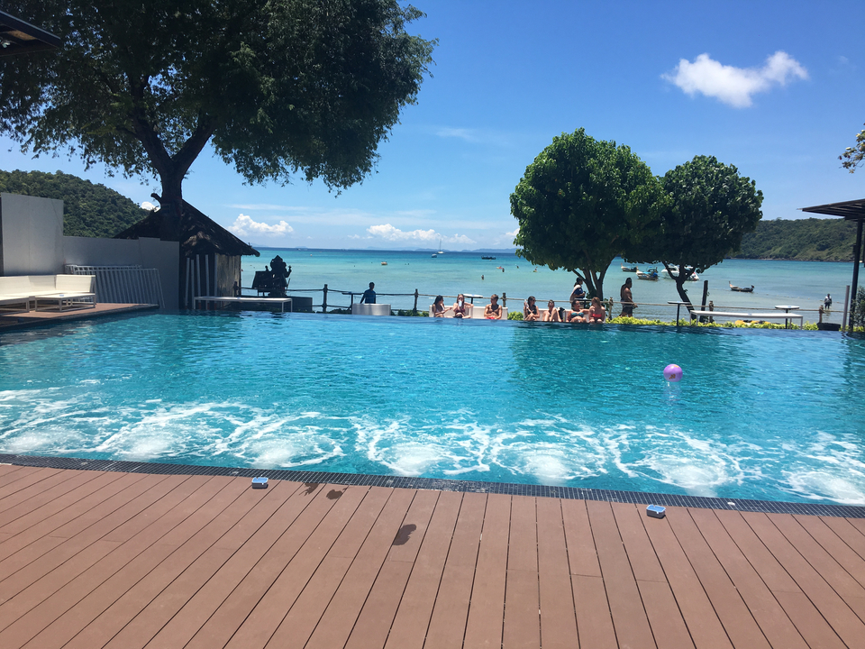 Mixed group of people relaxing by a modern swimming pool with sea view.