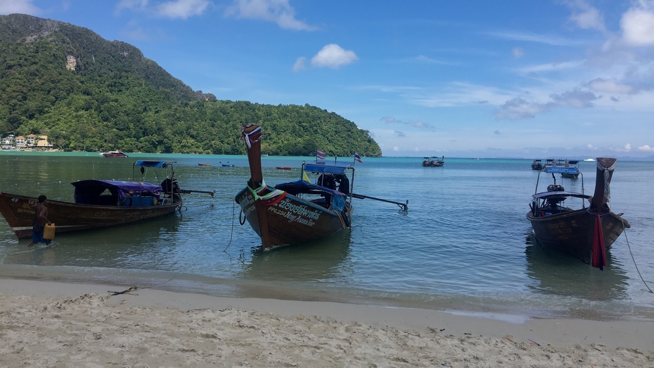 Wooden boats anchored on a serene beach with lush hills in the background.