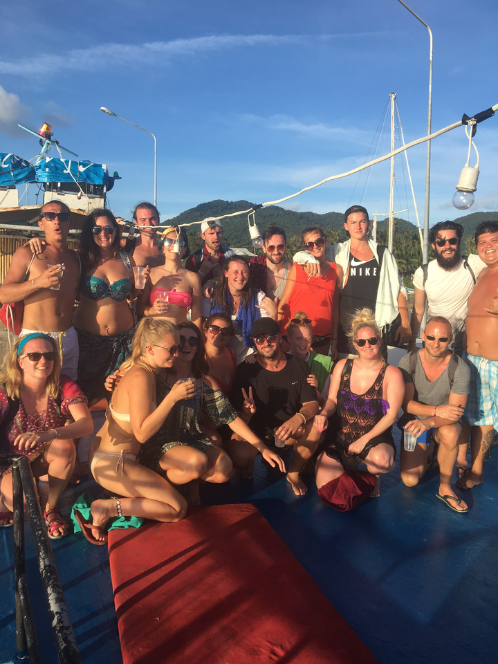 A group of people posing on a boat with lush greenery and hills in the background.