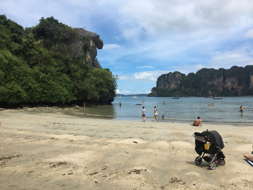 Beach with people swimming and a nearby stroller, surrounded by rock formations.