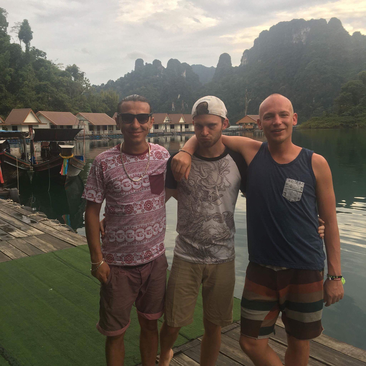 Three friends posing on a lakeside dock with traditional houseboats.