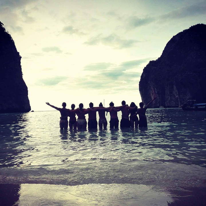 Group of friends in the water with backs to the camera facing cliffs.