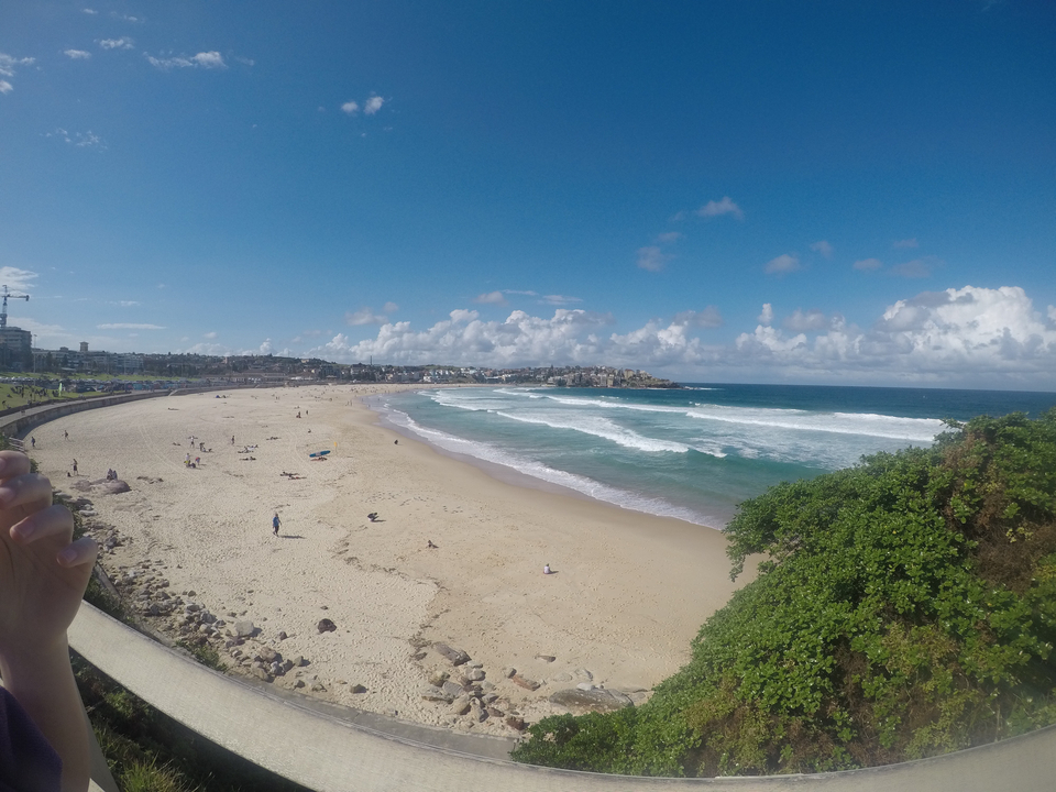 Beach scene with waves, sand, and distant buildings.