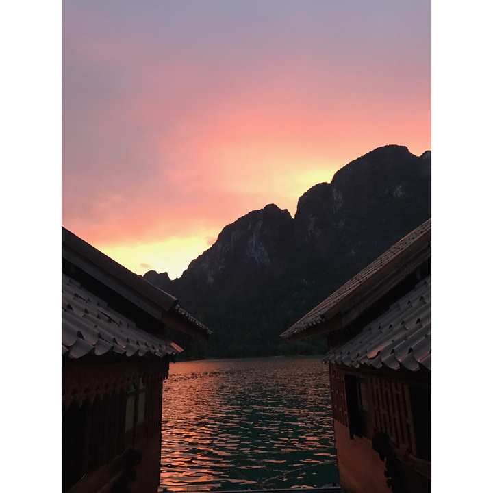 Sunset over mountains with rooftops in the foreground.