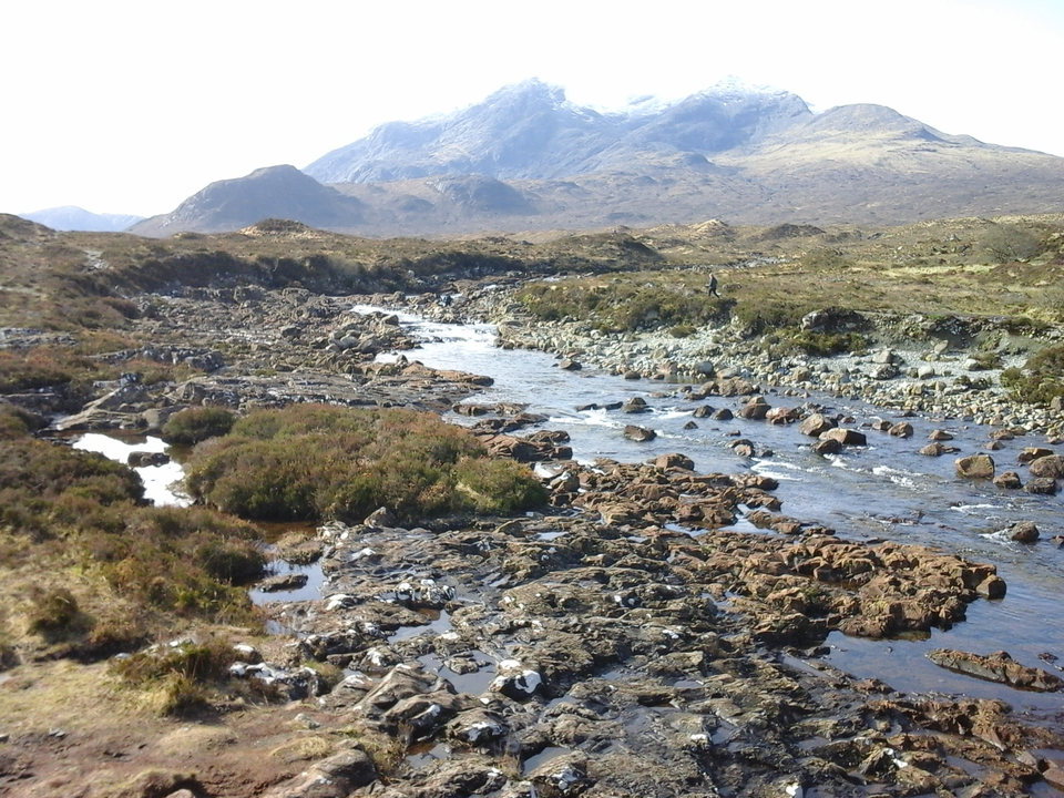 Rocky river landscape with mountains in the distance under a clear sky.