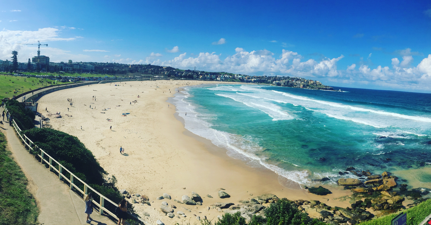 Panoramic view of a sandy beach with turquoise waves and a distant town.
