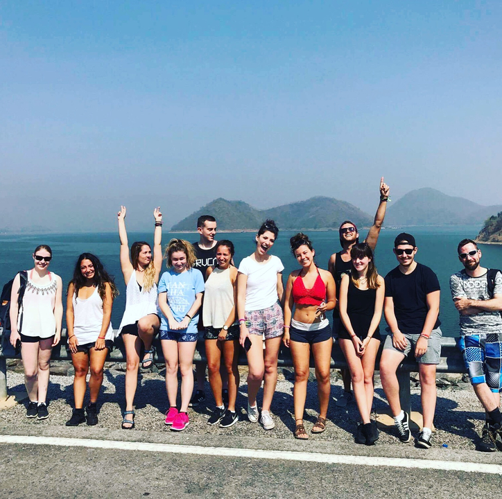 Group of tourists posing by a lake with mountains in the background.