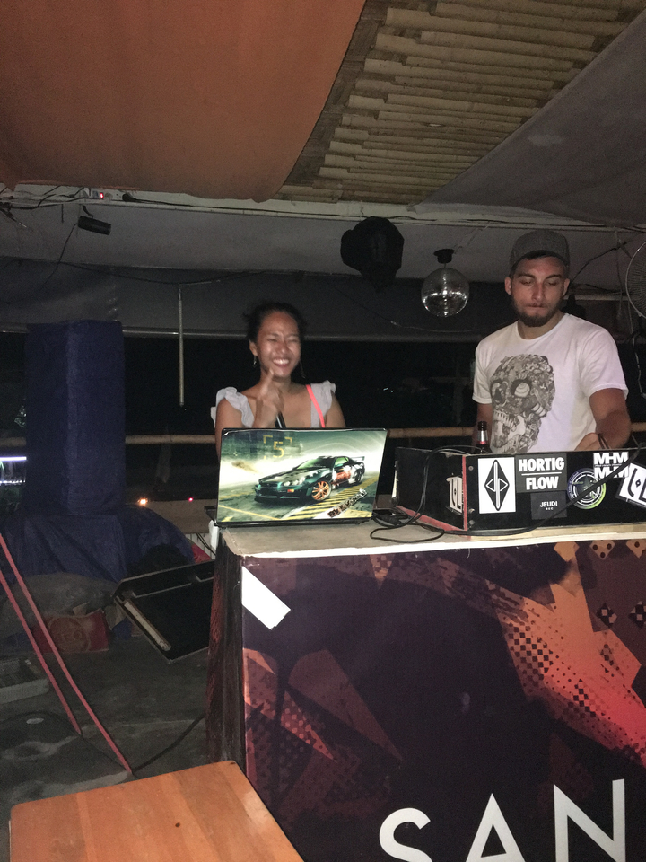 Two people working at a DJ booth in a dimly lit area.