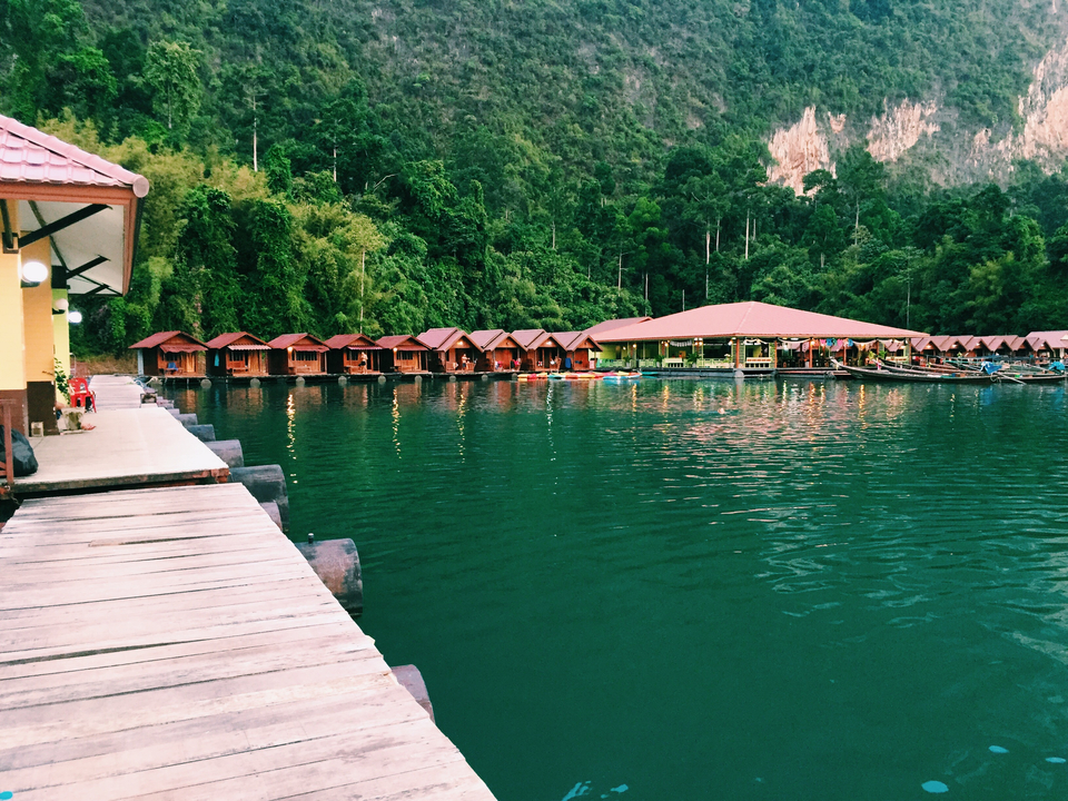 Floating raft houses on a lake surrounded by forested mountains.
