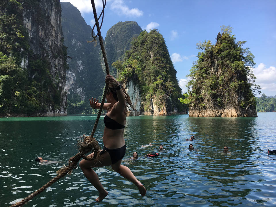 Person swinging over water with limestone karsts in the background.