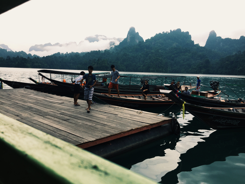 People boarding traditional boats on a lake surrounded by mountains.