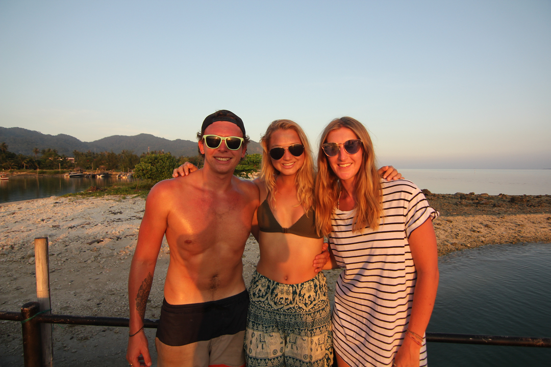 Three people posing on a rocky shore during sunset.