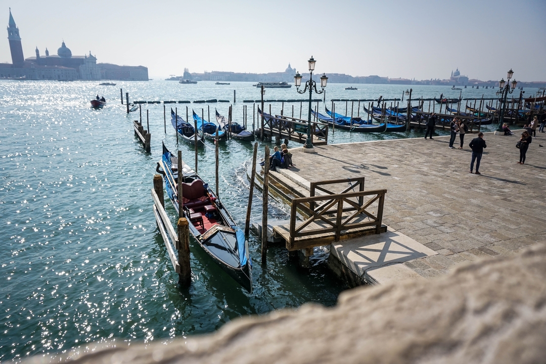 Gondolas docked by a boardwalk with a view of Venice's waterfront.