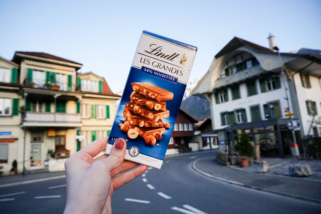 Hand holding a Lindt chocolate bar with buildings in the background.