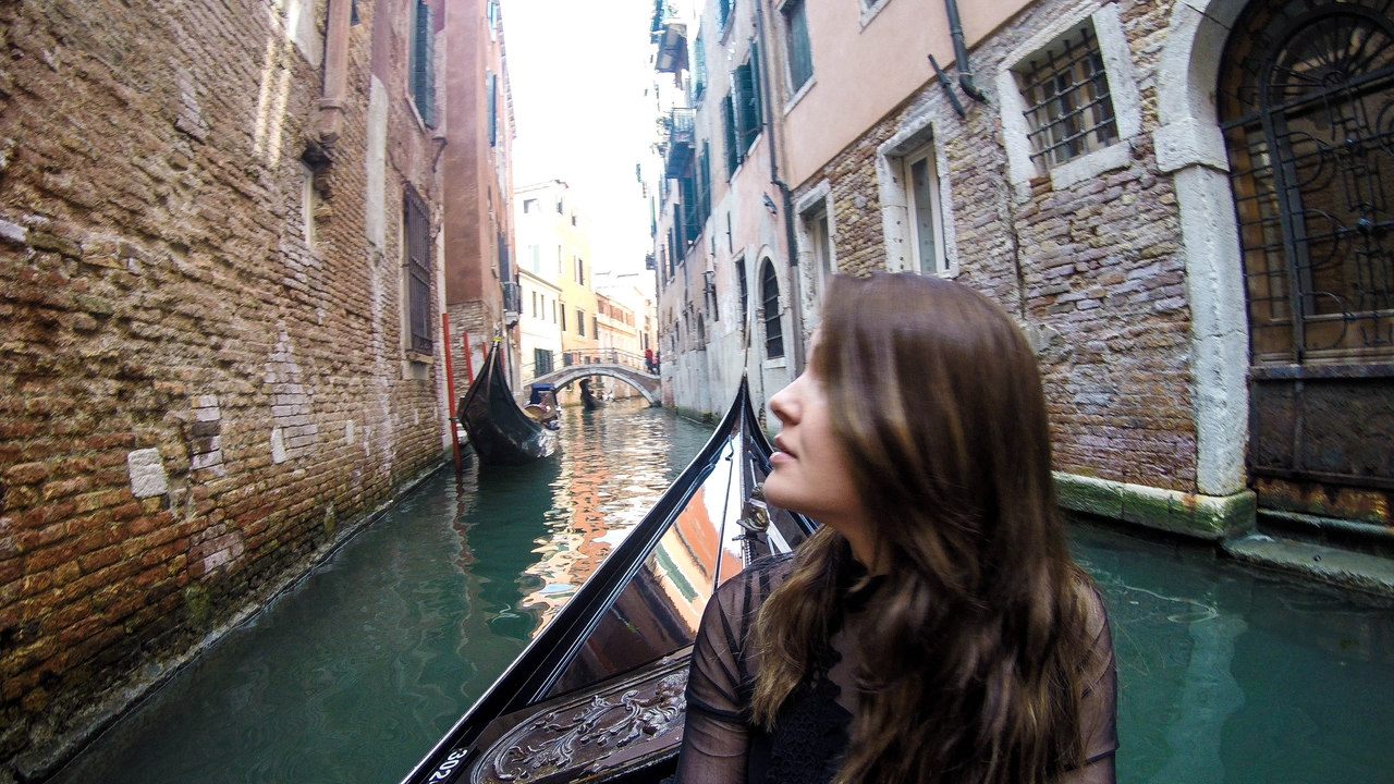 A woman in a gondola on a narrow canal in Venice.