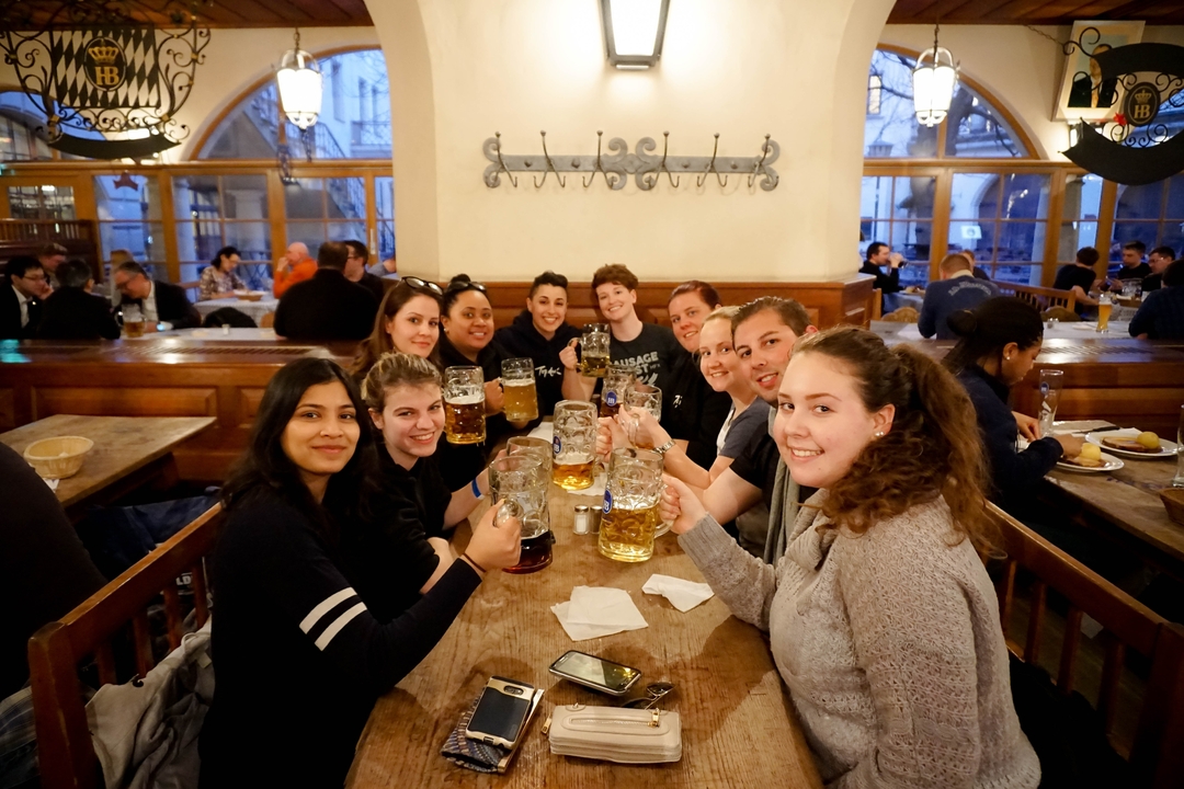 Group of people holding up beer mugs in a celebratory fashion at a table.