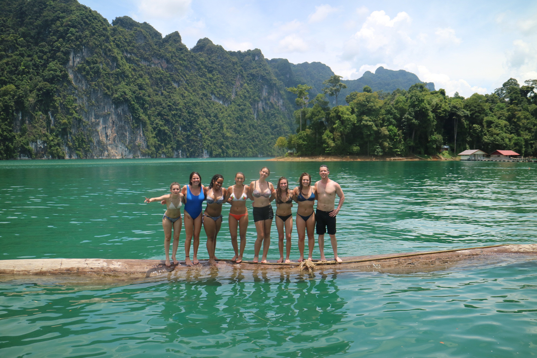 Cheerful group of people on a log floating in a lake.
