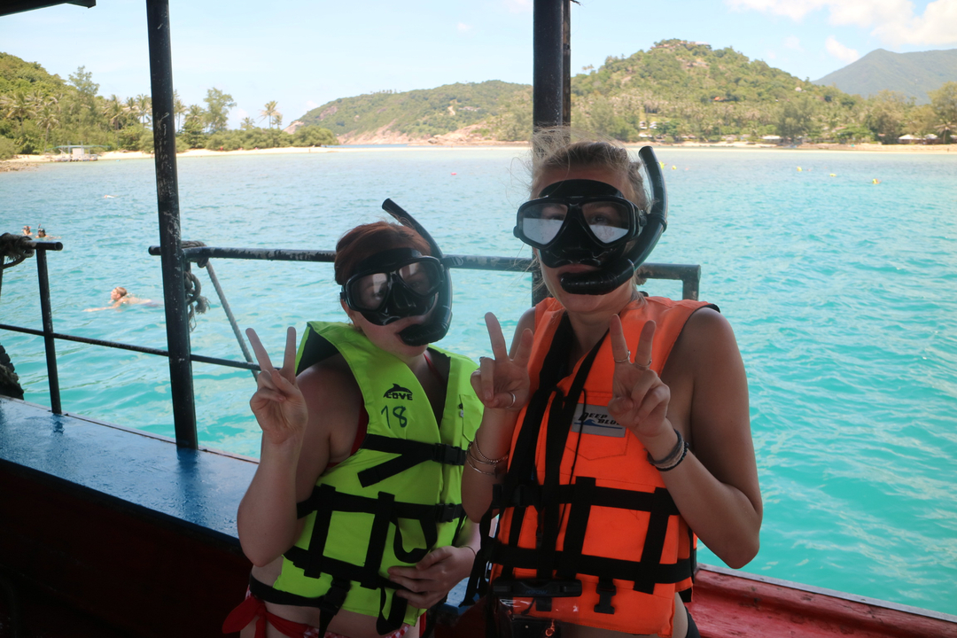 Two snorkelers smiling and posing on a boat with ocean backdrop.