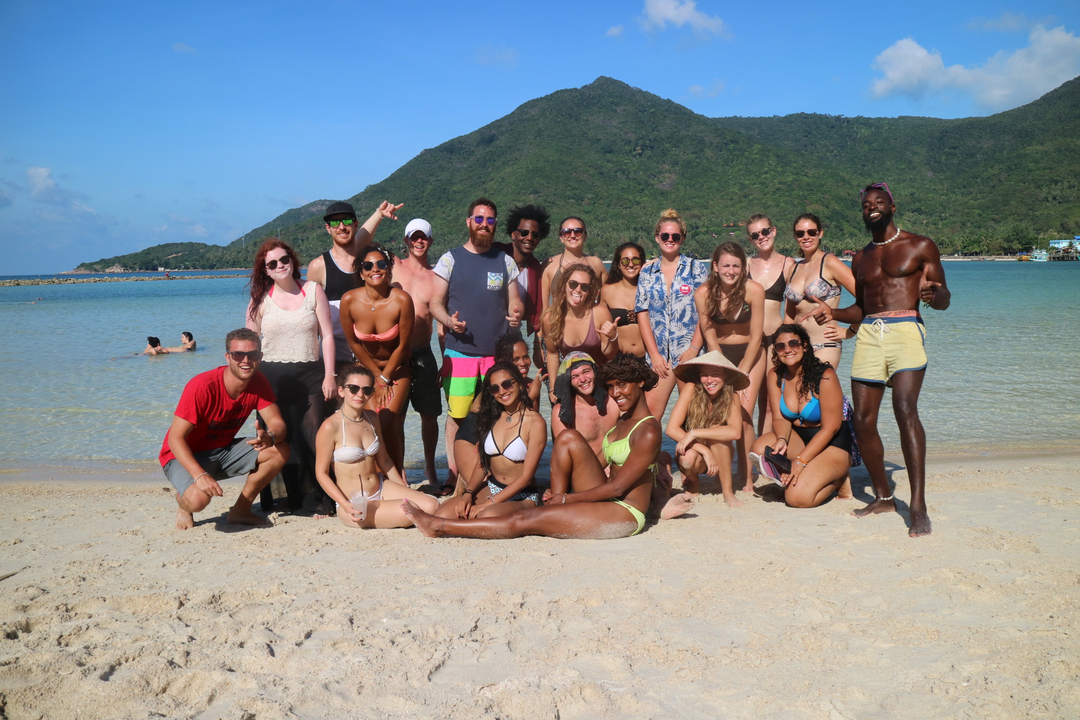 Group of people posing on a beach with mountains in the background.
