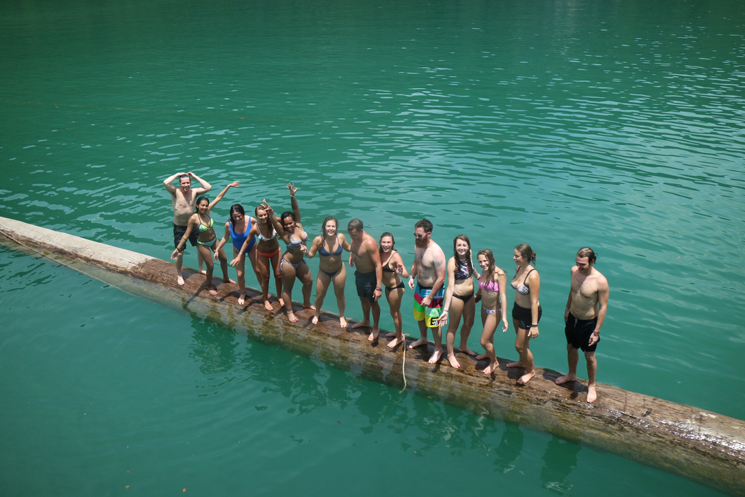 Group of people on a long log in clear blue water.