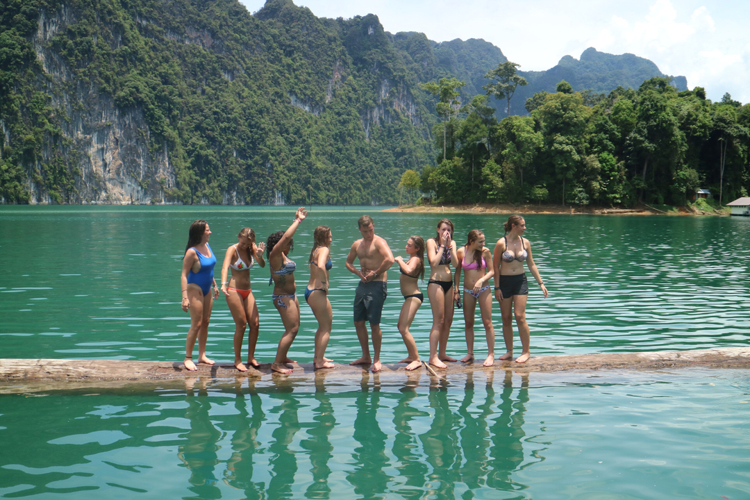 Group of people standing on a log in a lake.
