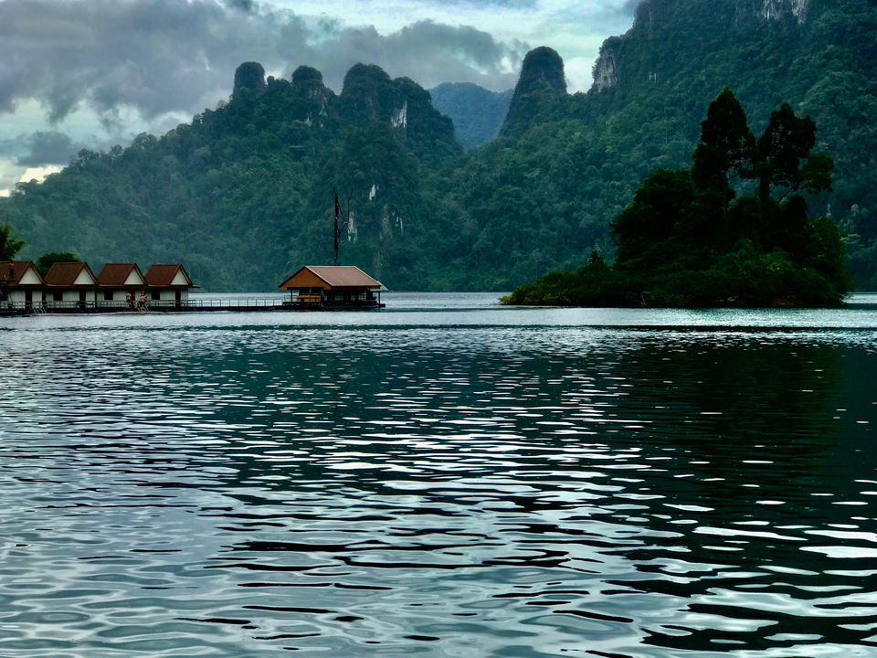 Lake view with thatched roof bungalows and forested hills.
