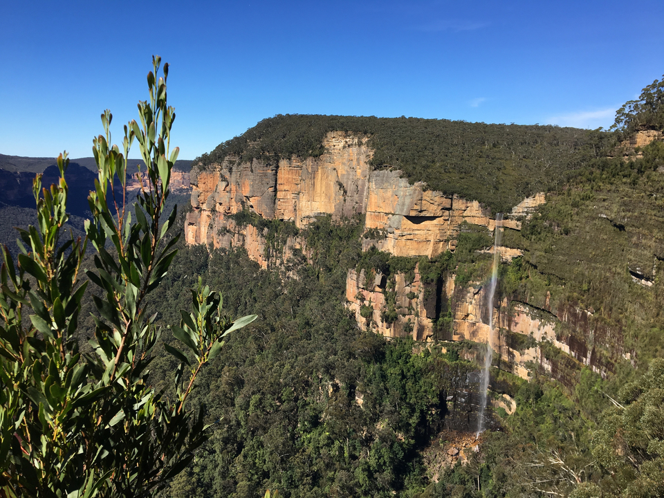 Rock cliff against blue sky with lush greenery and waterfall.