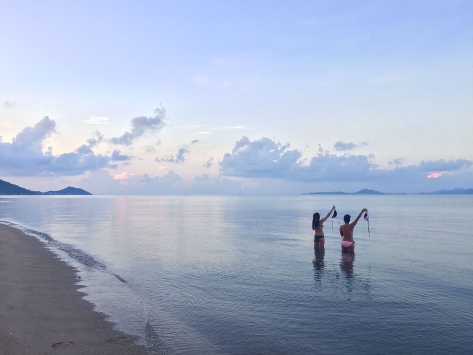 Two people in the water at sunset with a calm sea and cloudy sky.