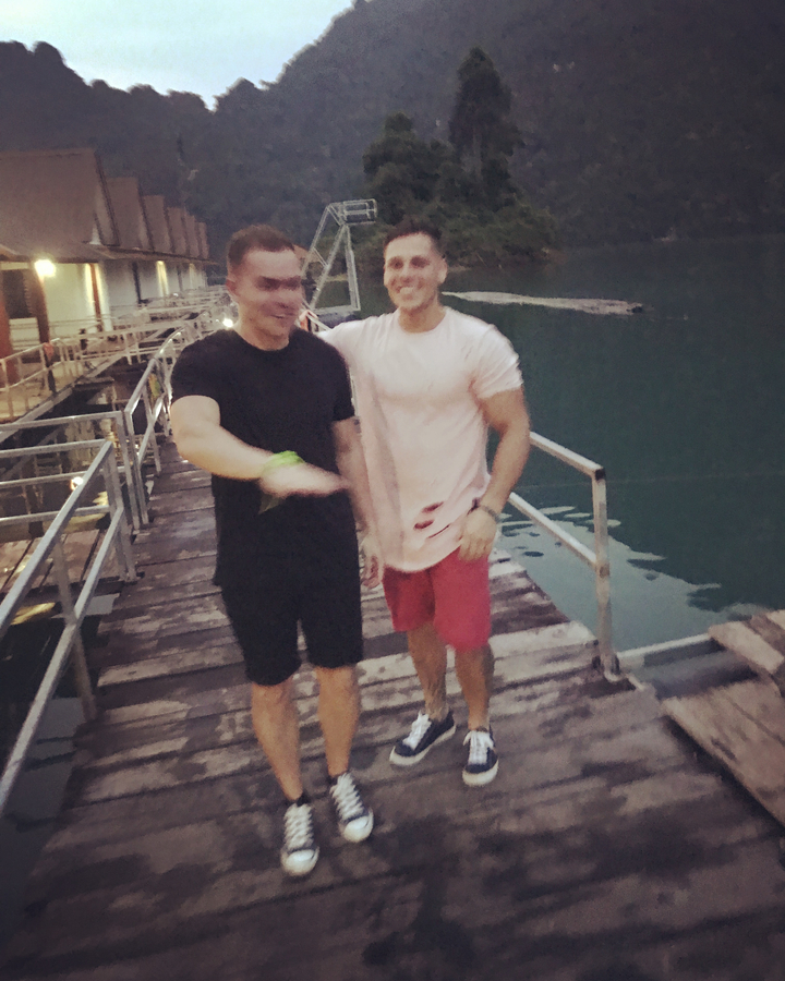 Two people walking on a wooden dock by the water.