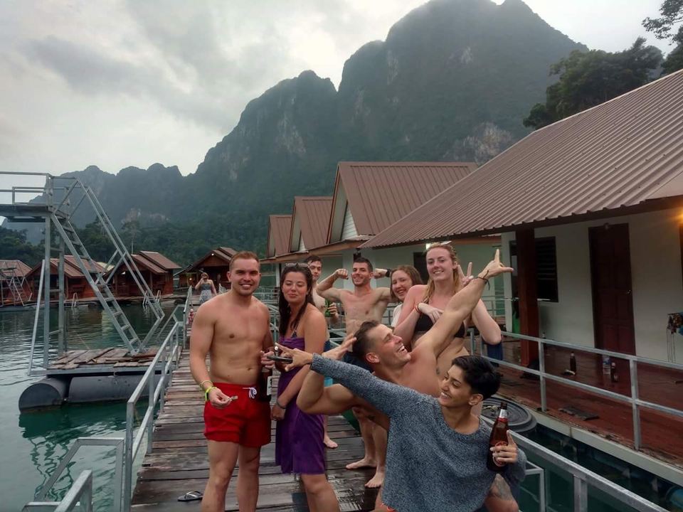 Group of people on a dock with houses and mountains.