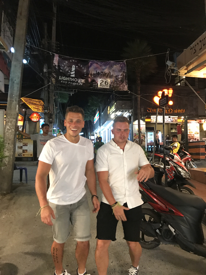 Two friends smiling on a bustling street at night.