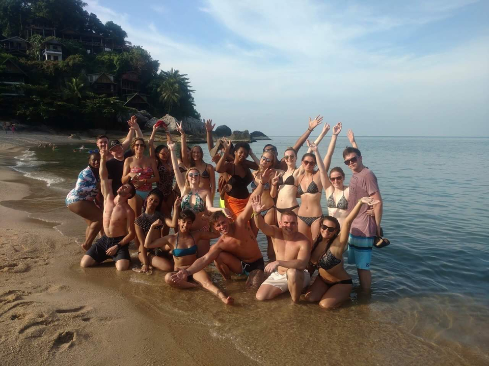 Group of people on a beach by the water, waving.