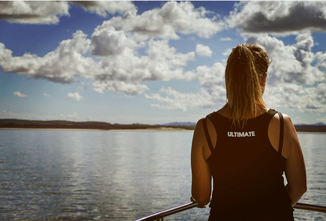 Person standing by the water, looking out with 'Ultimate' on their shirt.