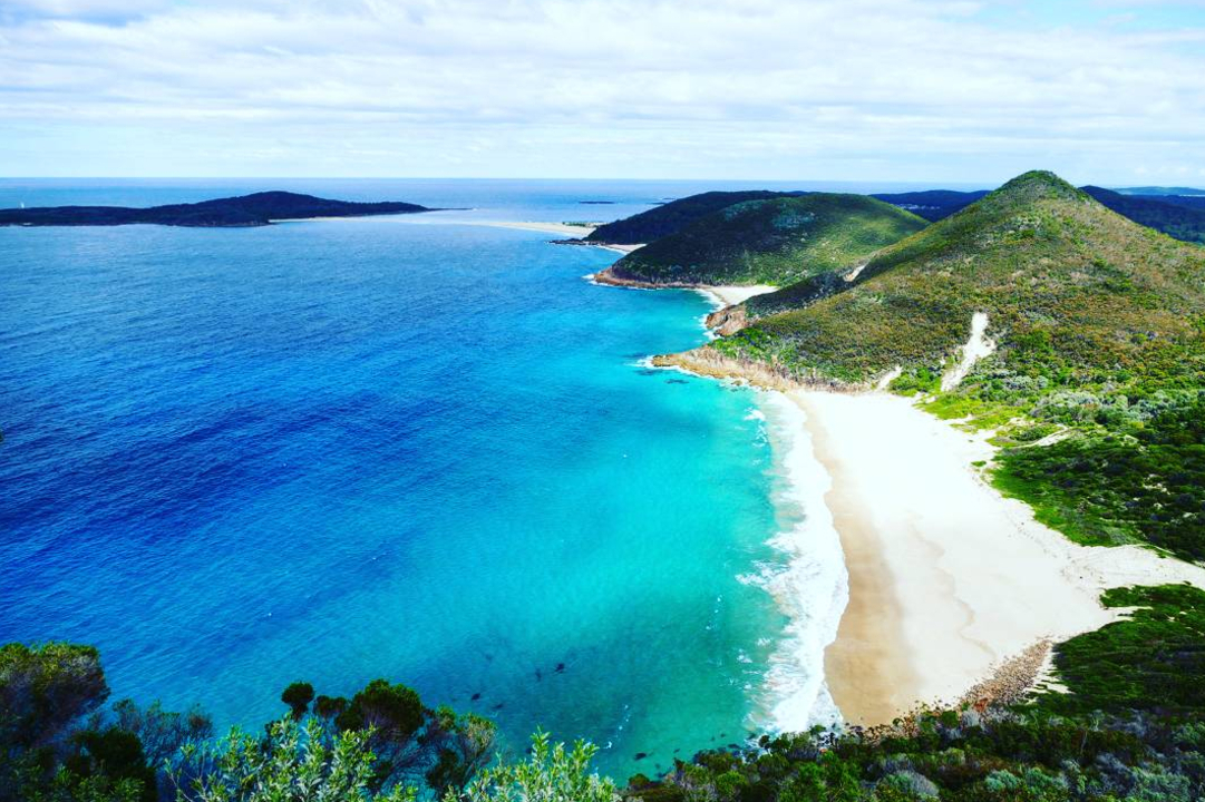 Aerial view of a coastline with clear blue water and mountains.