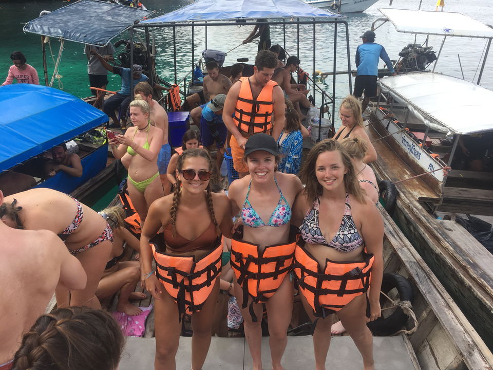 Group of people on a boat in life vests amidst clear water.