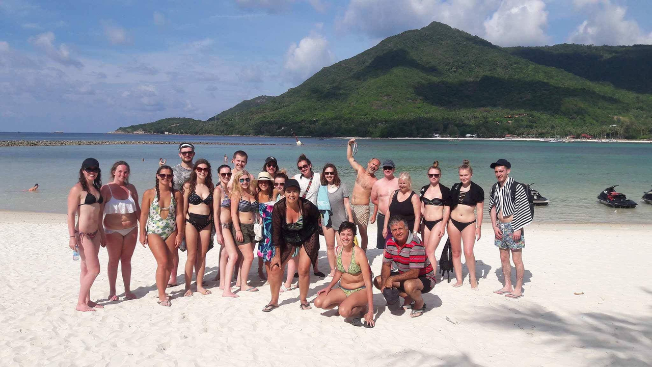 Large group on a sandy beach with a backdrop of hills.