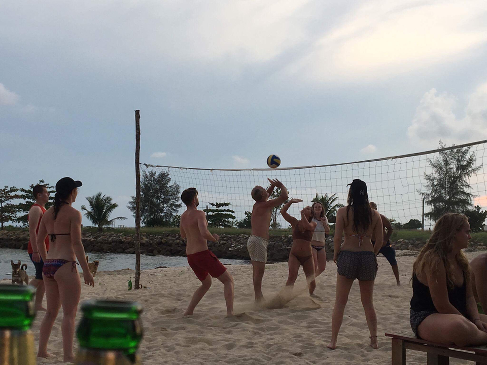 People playing beach volleyball with a net on a sandy shore.