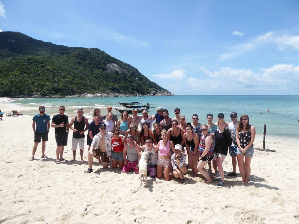 Large group posing on the beach with hills and clear skies.