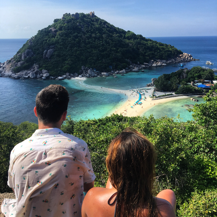 Couple looking at a beach with turquoise water from an elevated view.