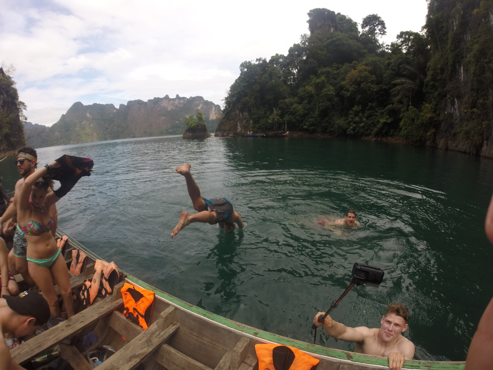 People swimming and diving into the water from a boat with mountains in the background.