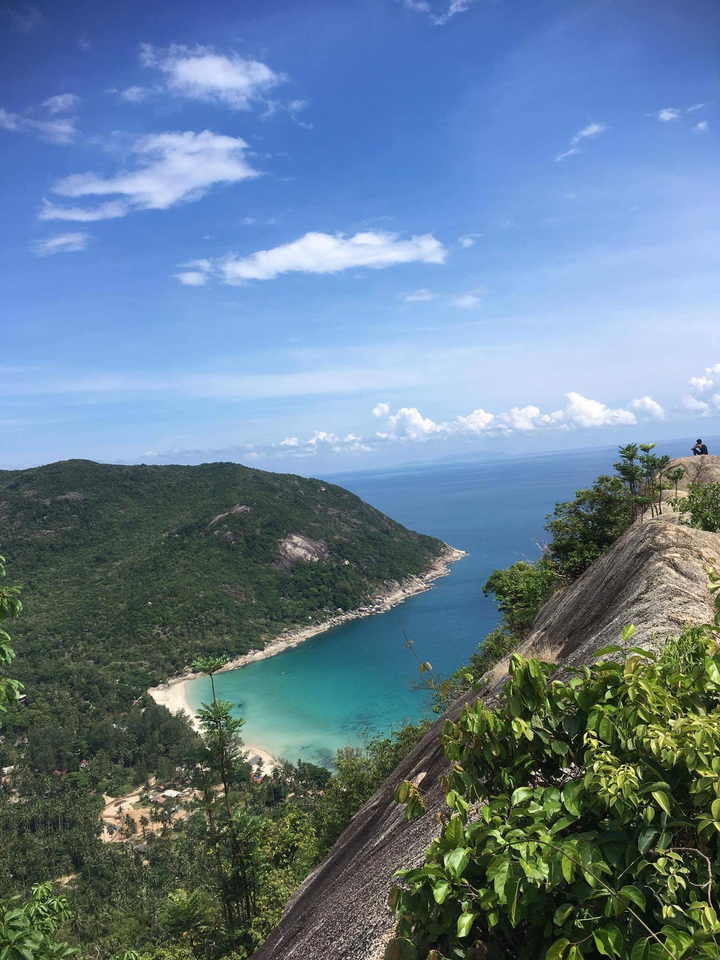 Scenic coastal view with a person sitting on a rocky cliff.