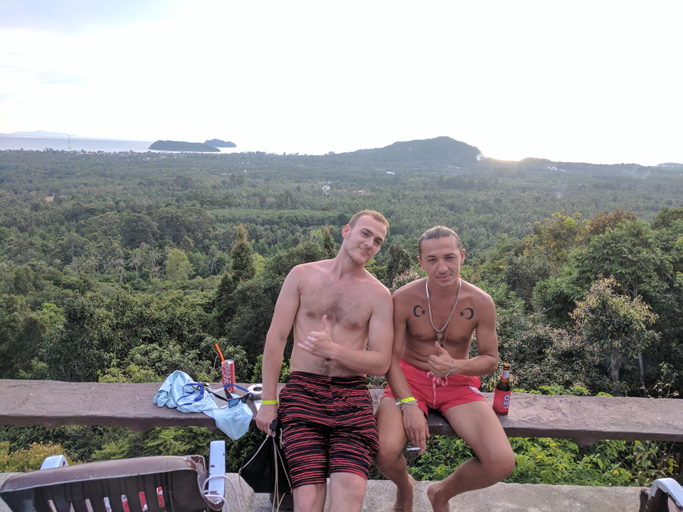 Two men sitting and smiling with a panoramic view of trees and hills.