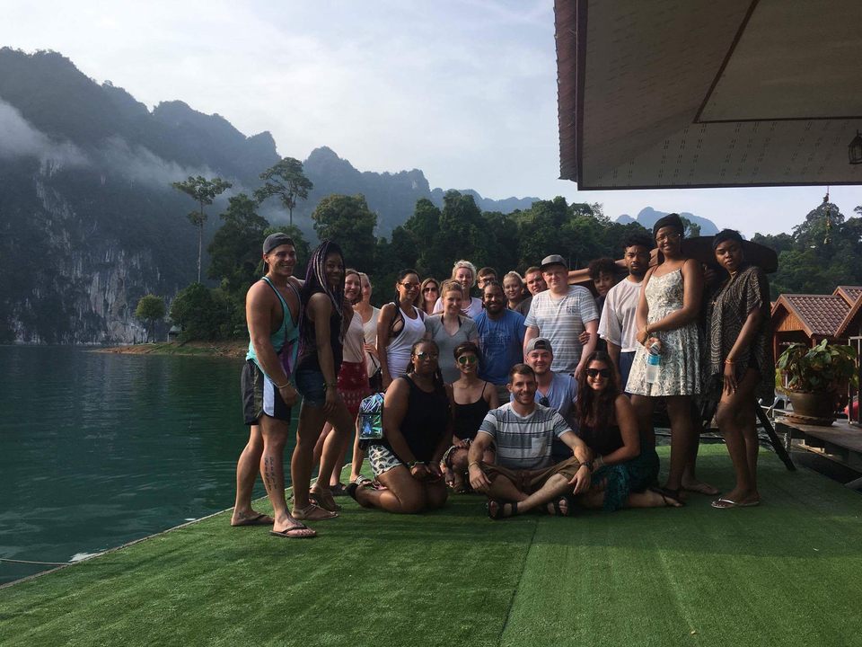 Group of people posing on a dock with scenic lake and mountains.
