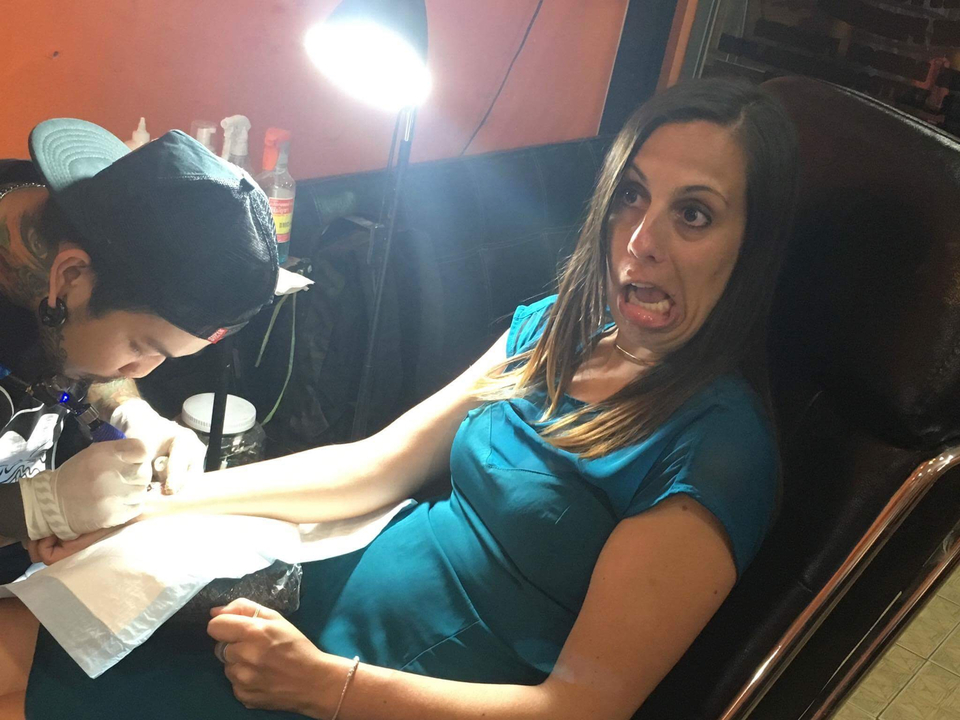 Woman getting a tattoo in a tattoo parlour with an expressive face.