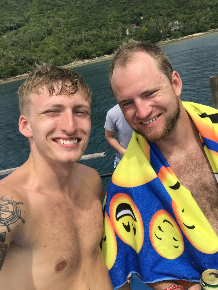 Selfie of two men smiling on a boat with water in the background.