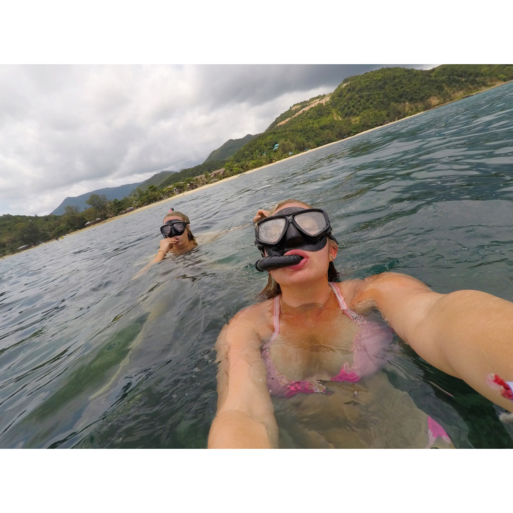 Two people snorkeling in the ocean near a tropical island.