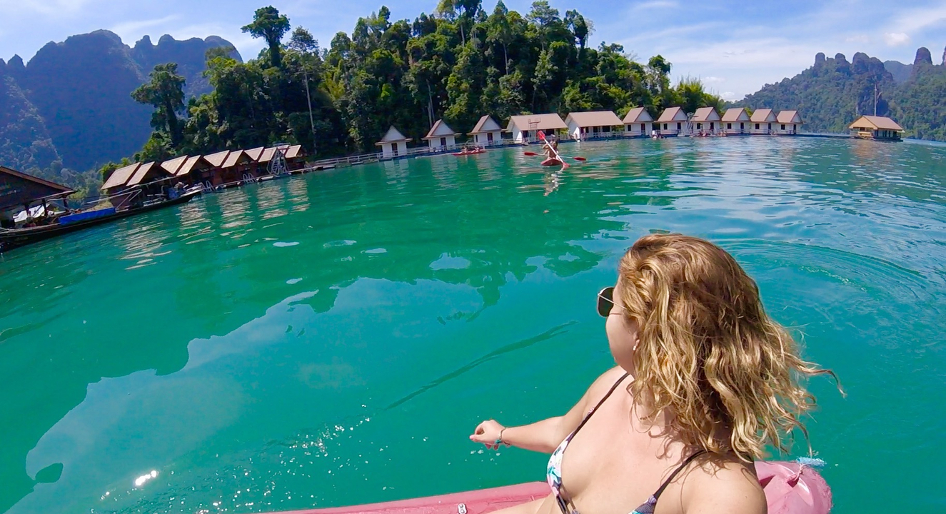 Woman kayaking with floating bungalows on a clear lake.