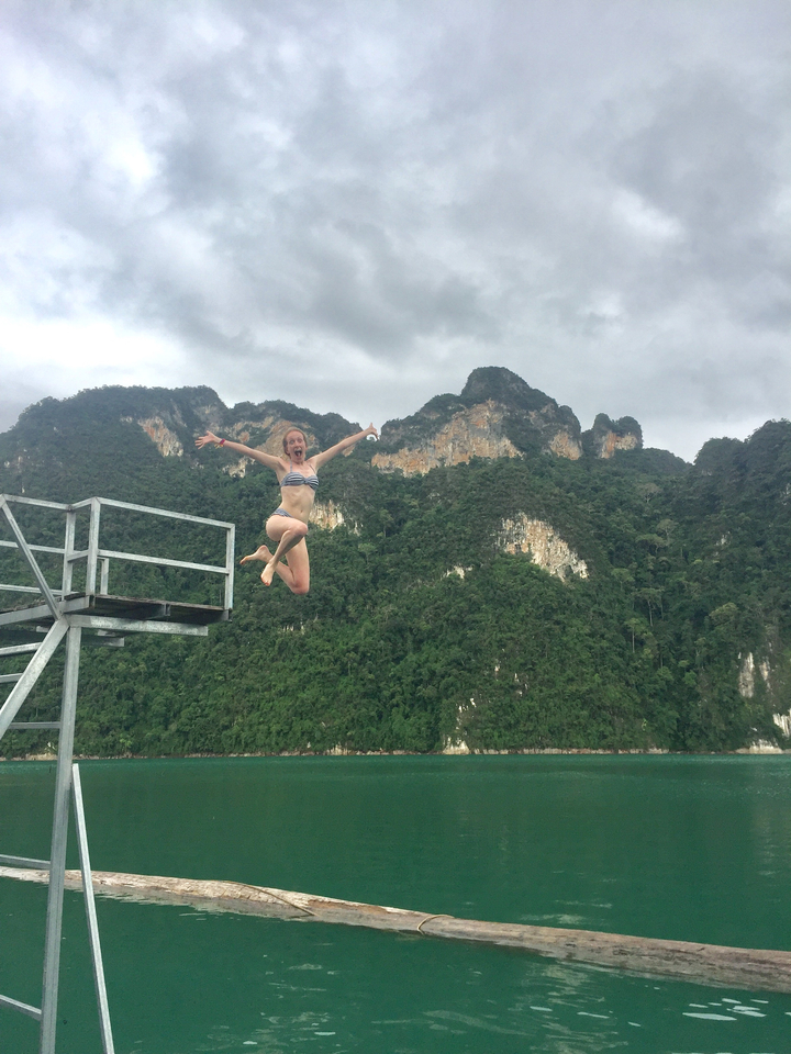 Woman jumping off a diving platform with lush mountains behind.