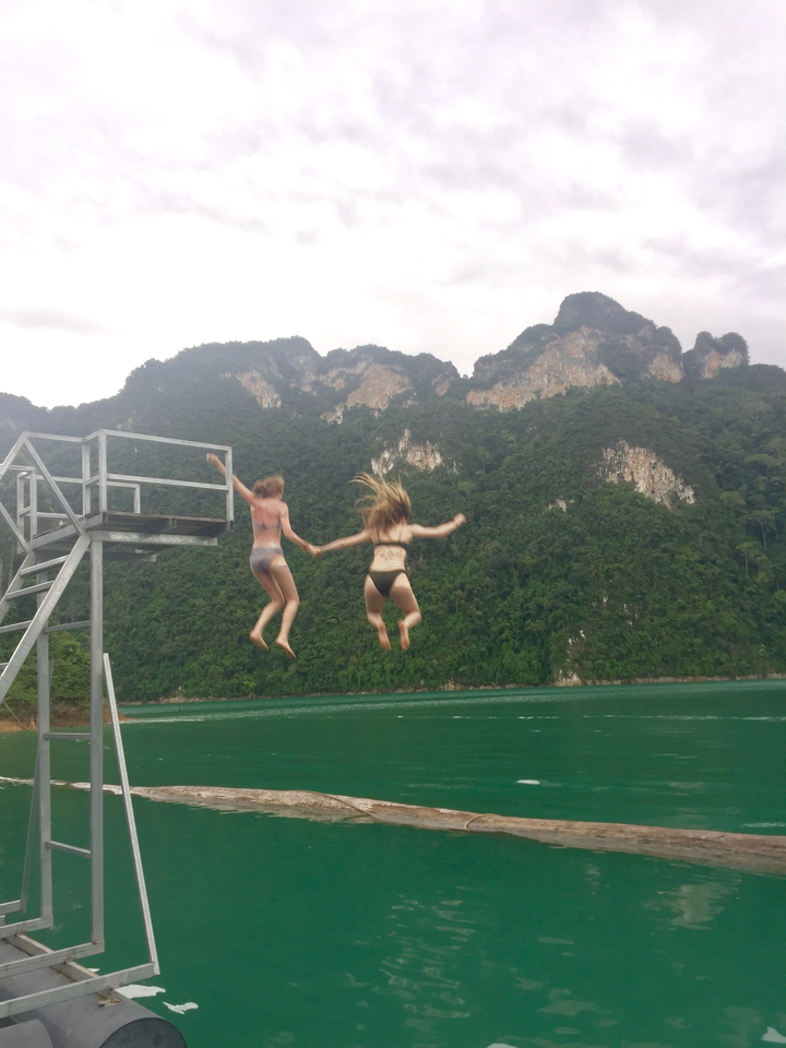 Two women jumping hand in hand from a platform into a lake.