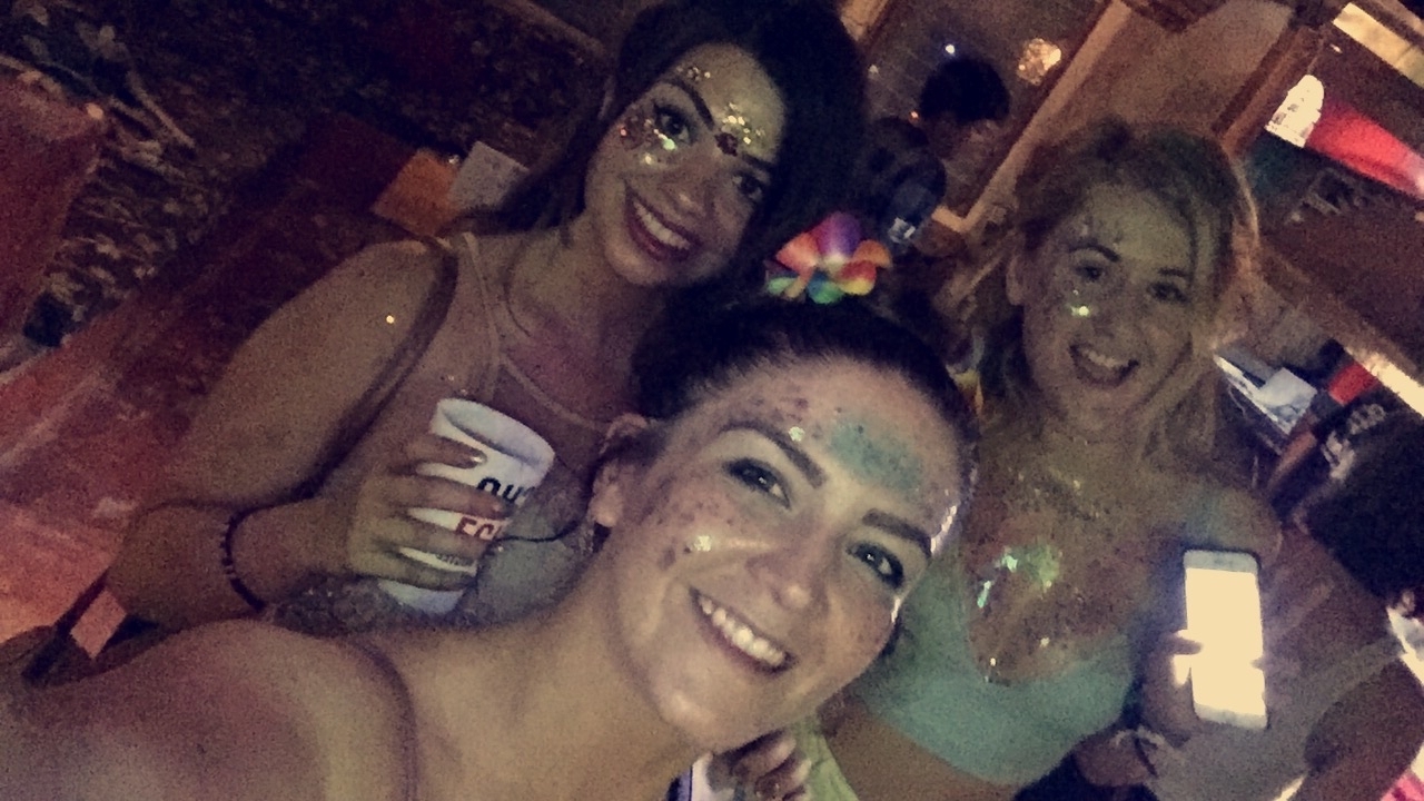 Three people with glitter makeup enjoying a party.